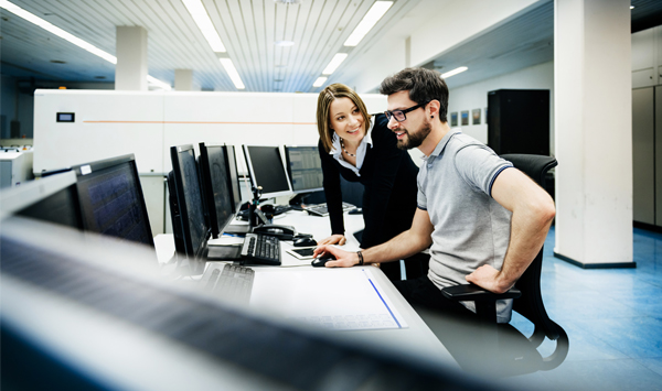 Zwei Büroangestellte sitzen am Computer und besprechen sich. 