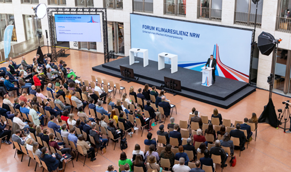 Blick von oben auf das Publikum und die Bühne. Am Rednerpult auf der Bühne steht NRW-Umweltminister Oliver Krischer.