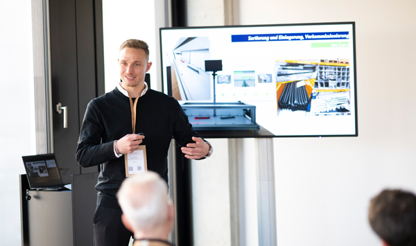 Ein Mann steht vor dem Publikum und präsentiert eines der KI-Pilotprojekte