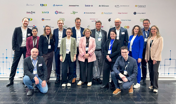 Ein Gruppenbild mit 15 Personen die auf der Hannover Messe vor einer Projektwand stehen.