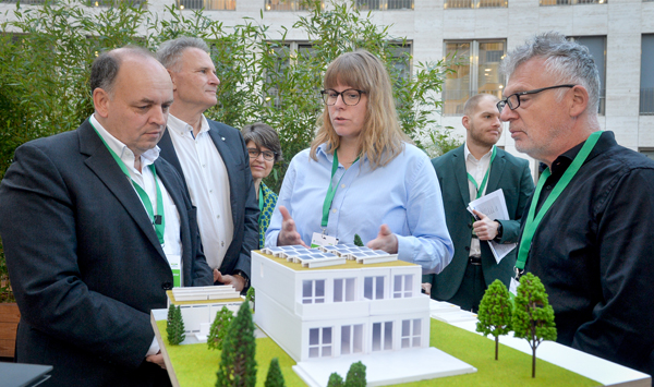 Teilnehmende des Summits betrachten ein Hausmodell zum seriellen und zirkulären Bauen.