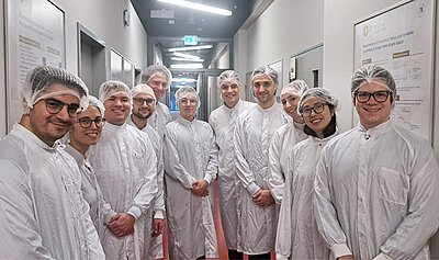 Die Finalisten des Quantum Future Awards bei einer Laborführung. Sie tragen Labokittel und Haarnetze. 