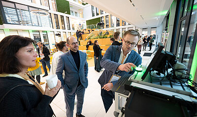 Ein Mann präsentiert zwei interessierten Personen ein KI-Projekt am Computer