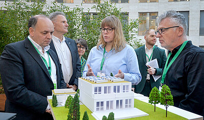 Teilnehmende des Summits betrachten ein Hausmodell zum seriellen und zirkulären Bauen.