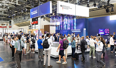 Besucherinnen und Besucher stehen am Messetand des Bundesforschungsministeriums auf der World of Quantum