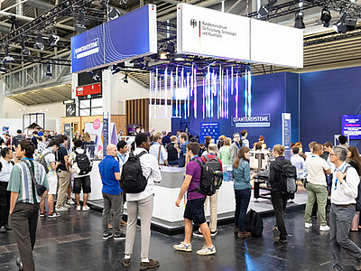 Besucherinnen und Besucher stehen am Messetand des Bundesforschungsministeriums auf der World of Quantum